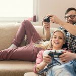 couple-in-love-enjoying-their-free-time-sitting-on-a-couch-next-to-the-window-playing-video-games-and-having-fun-lens-flare