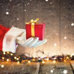 santa-claus-hand-holding-christmas-gift-box-over-wooden-background-proposing-product-advertisement-gesture-presenting-point-deco